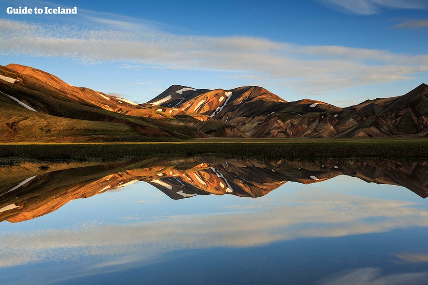 Landmannalaugar rhyolite mountains in Iceland reflected in calm water at sunset with vivid summer colors.