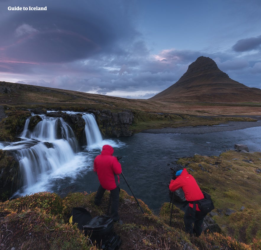 People taking photos of Kirkjufellsfoss waterfall with Kirkjufell mountain in the background.