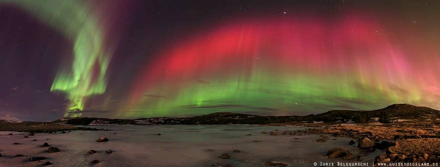 Wide panorama of green and red northern lights over Iceland during a night of high aurora activity.