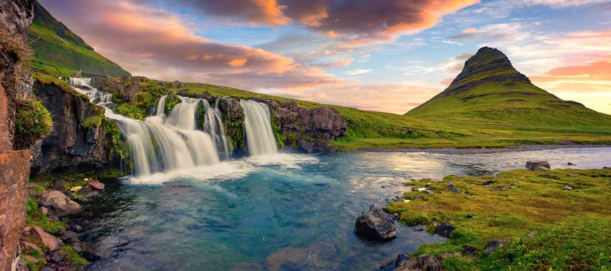 Kirkjufellsfoss flows in the foreground as evening light falls on Kirkjufell.
