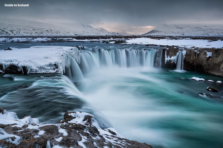 Snow and ice partially cover the Godafoss waterfall in winter.