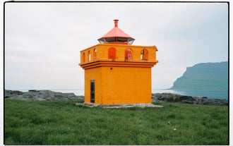 Ein kleiner, leuchtend orangefarbener Leuchtturm bildet einen schönen Kontrast zur atemberaubenden Naturlandschaft des Seydisfjördur-Fjords.