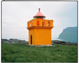 Un piccolo faro arancione brillante contrasta meravigliosamente con lo scenario naturale mozzafiato del fiordo di Seydisfjordur