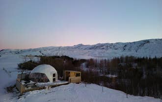Stay warm in the cozy Eyja Mork glamping dome, evening amid snow-covered surroundings.
