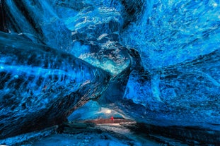 A traveler stands inside the Crystal Ice Cave in Vatnajokull Glacier, Iceland, beneath glowing blue ice walls.