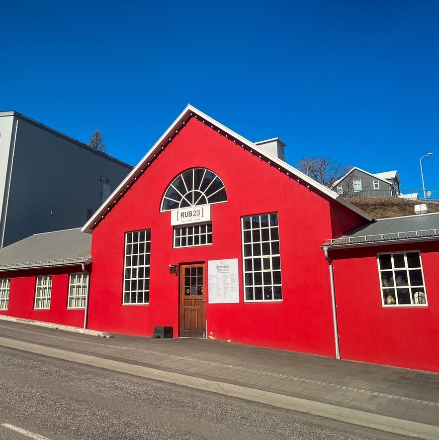 Bright red exterior of Rub 23 restaurant in Akureyri, Iceland, housed in a historic building with large windows and a central arched entrance.