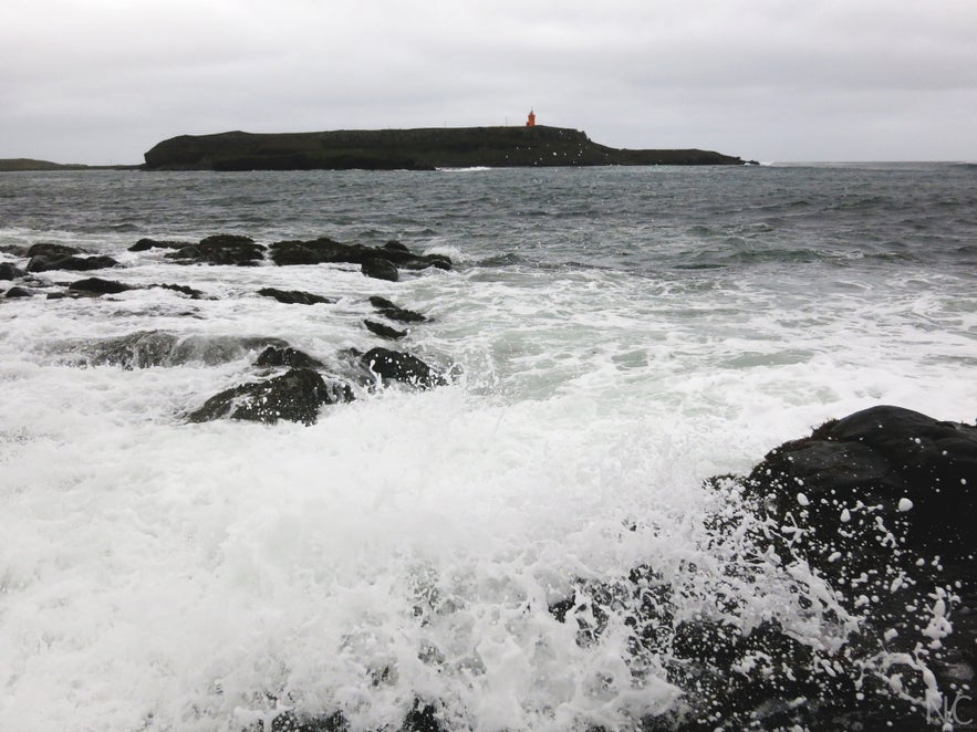 A black and white photo of Raufarhofn coastline with the lighthouse on the cliff in orange.