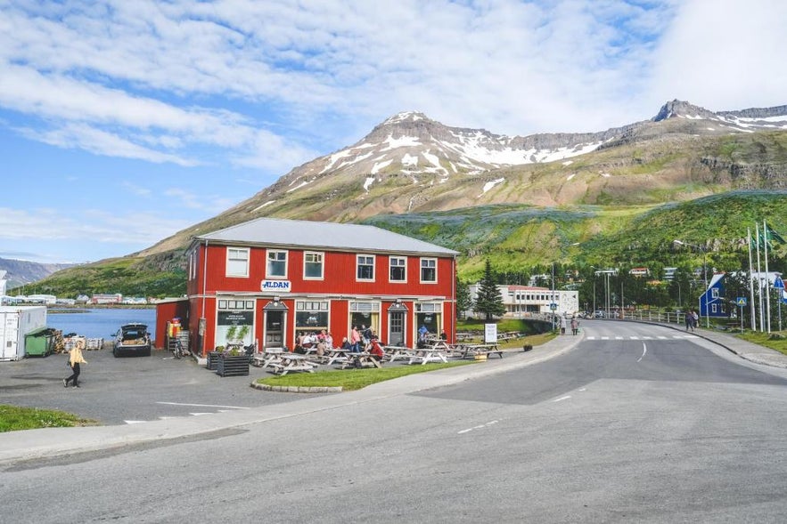 Hotel Aldan in Seydisfjordur, Iceland with outdoor seating, fjord views, and snow-capped mountains in the background.