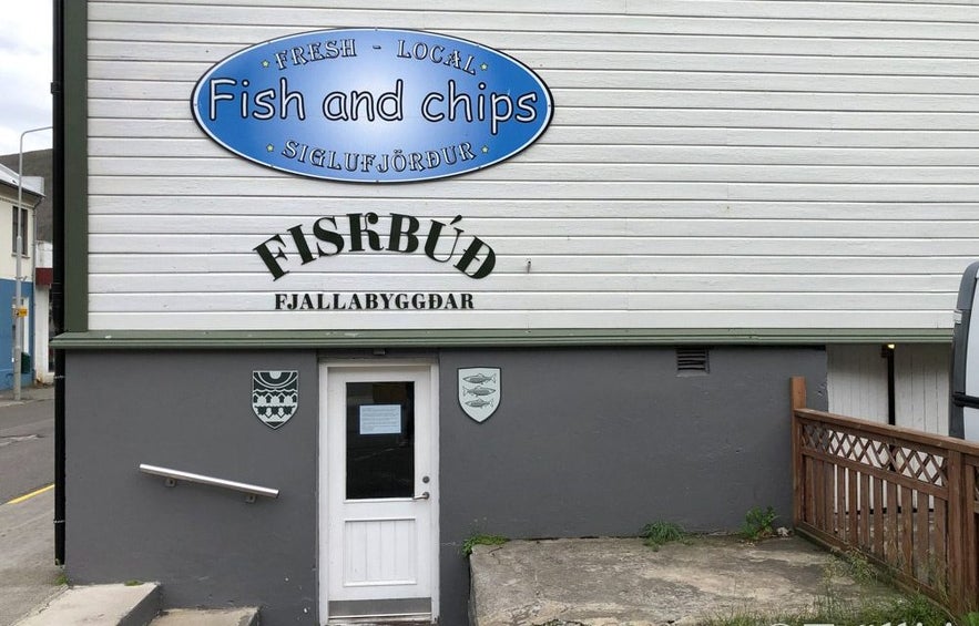 Entrance to the Fish and Chips shop in Siglufjörður, Iceland, located in a modest building with signage reading “Fresh • Local • Fish and Chips” above the door.