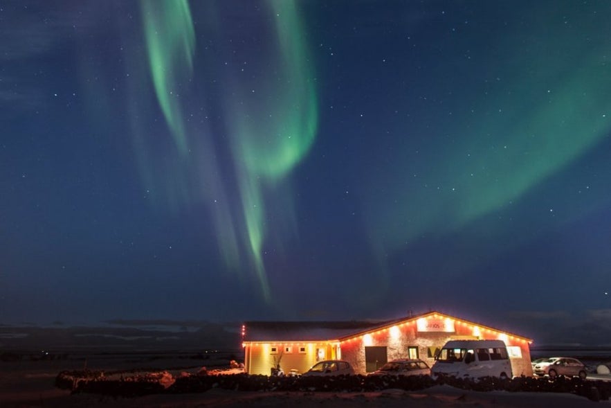 Vogafjós restaurant and guesthouse near Lake Mývatn, Iceland, illuminated at night with the northern lights dancing across the sky above.