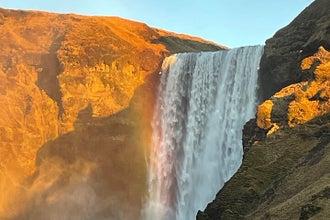 The side profile of a majestic waterfall basked in the warm glow of sunrise.