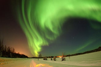 A vibrant spectacle of green auroras arches over a snowy Icelandic landscape, offering a stunning visual symphony of the Northern Lights near Reykjavik.