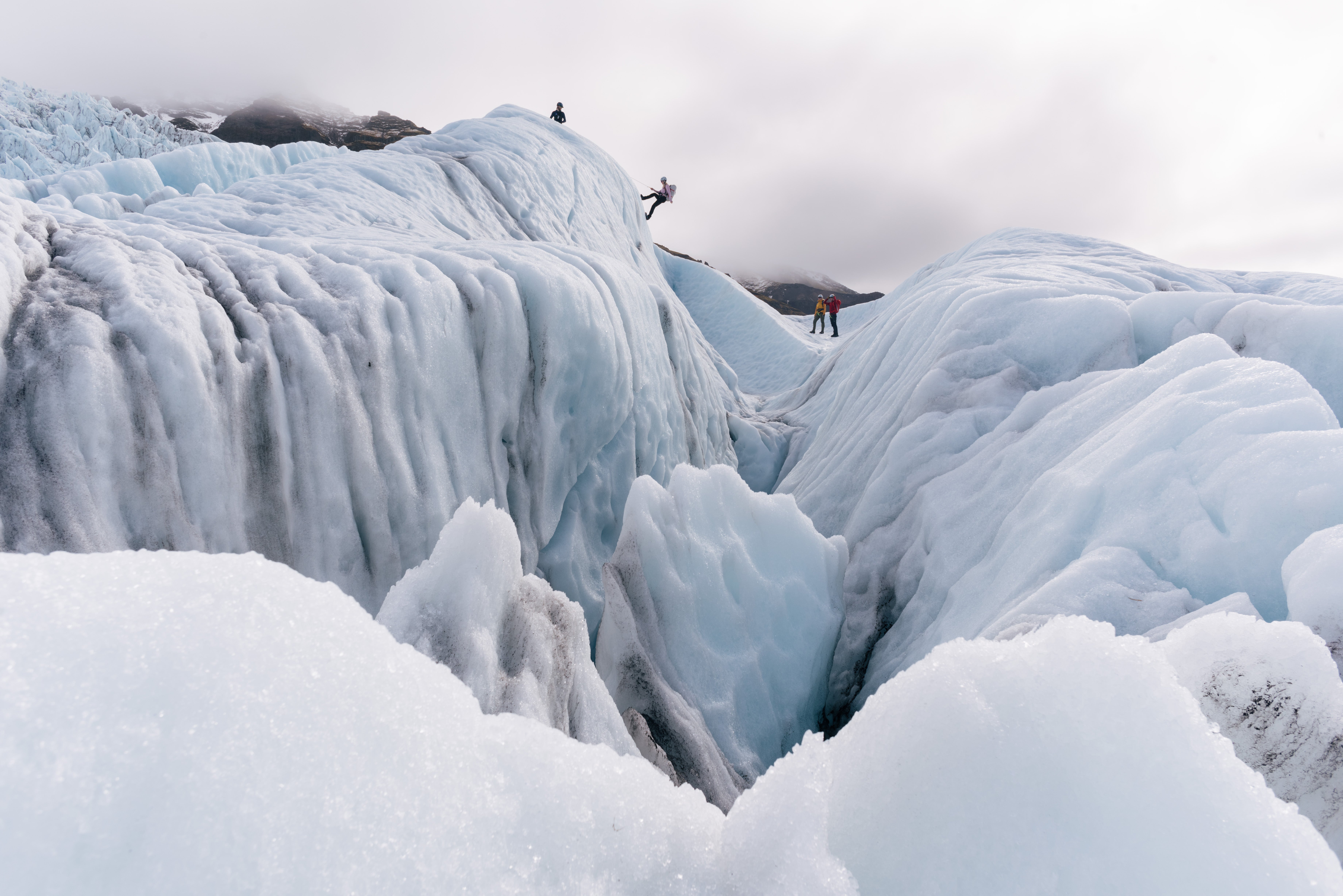 Dramatic peaks and cracks in a glacier in Iceland, with people descending one of the slopes on an ice-climbing tour.