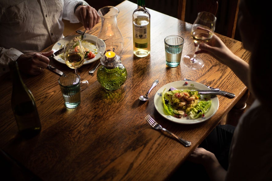 Two people dining at Hotel Siglunes restaurant in Siglufjörður, enjoying wine and a beautifully plated seafood dish by candlelight.