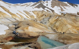 People on a helicopter tour explore the Kerlingarfjoll area in the Icelandic Highlands during a mountain landing next to a lake.