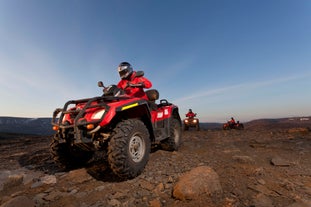 People drive ATVs over Iceland's rugged terrain with a backdrop of snowy mountains.