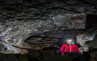A smiling person wearing a helmet and head torch explores the Leidarendi lava cave near Reykjavik.