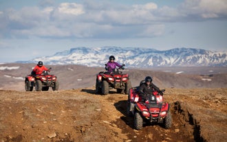 People drive ATVs over Iceland's rugged terrain with a backdrop of snowy mountains.