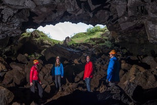 People wearing helmets and flashlights stand inside a lava cave with the light shining in from above.