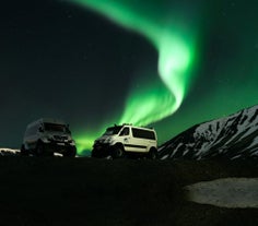 A display of the northern lights shines over two super jeeps in Iceland.