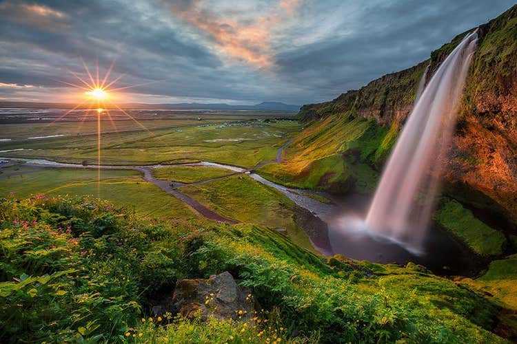 The midnight sun balances on the horizon before Seljalandsfoss waterfall on the South Coast of Iceland.