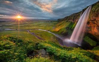 The midnight sun balances on the horizon before Seljalandsfoss waterfall on the South Coast of Iceland.