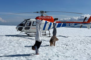 Two travelers doing a headstand beside a helicopter during a glacier landing.