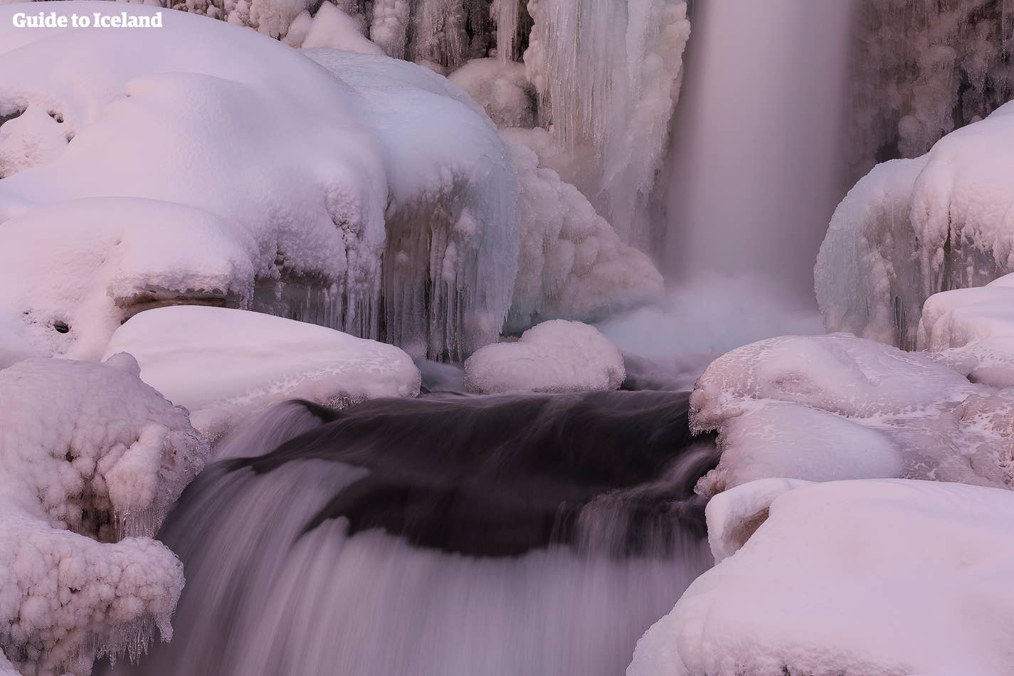 Een rozige wintergloed hangt over een met ijspegels gevulde waterval in IJsland