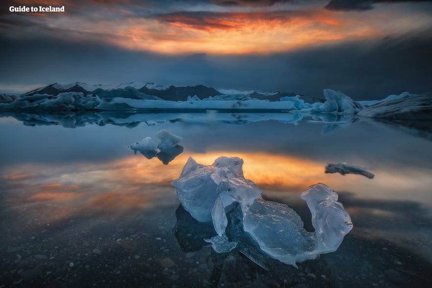 Sunset reflecting over Jokulsarlon Glacier Lagoon in South Iceland, with floating icebergs and calm mirror-like water.