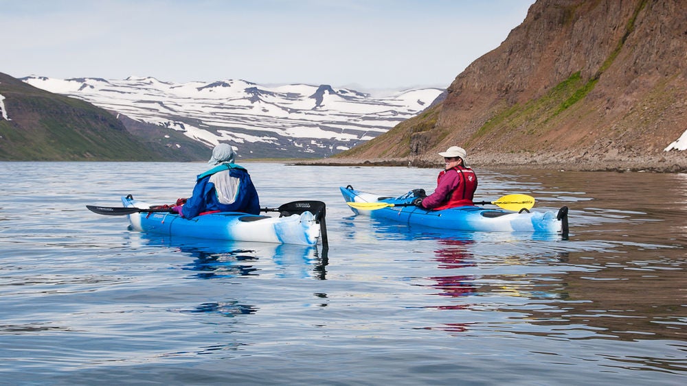 Two people in kayaks in front of a mountainous backdrop in the Westfjords.