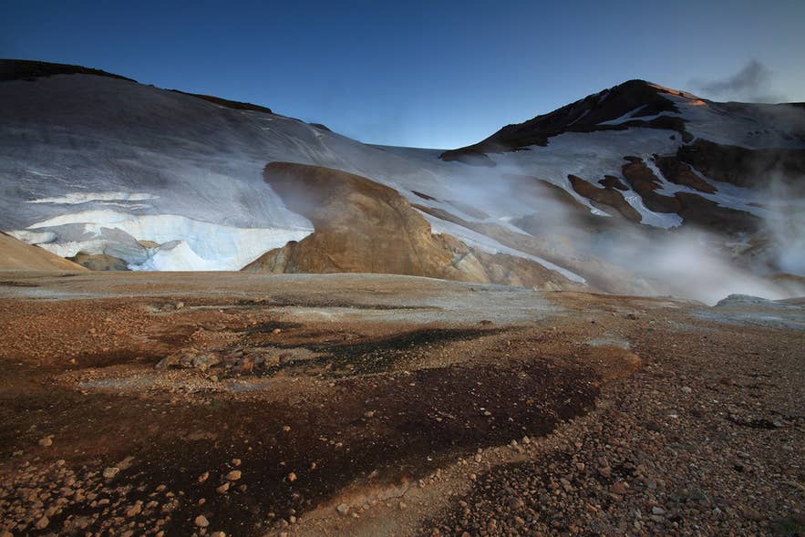 Vapore geotermico che si alza vicino al ghiacciaio Hofsjokull nelle Highlands islandesi, con neve e paesaggio vulcanico sotto cieli sereni.