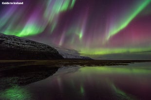 アイスランドの美しい湖の上空に、エメラルドと紫のオーロラが舞う。