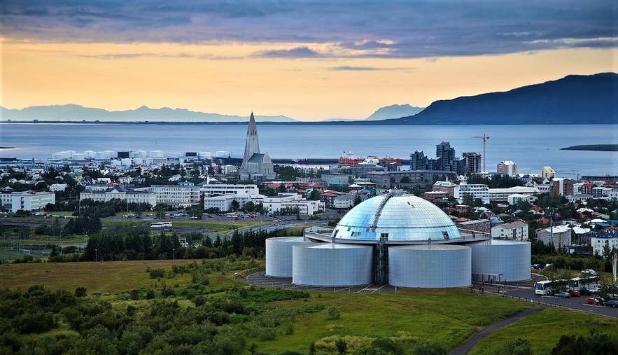 Perlan Museum in Reykjavik, a modern glass dome building on a grassy hill under a blue sky.