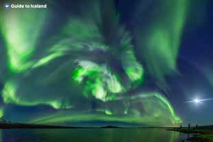 An ethereal ribbon of the Aurora Borealis weaves over the snow-covered banks of a peaceful river in the vicinity of Reykjavik.