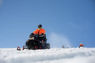 Une personne vêtue d'une combinaison orange et d'un casque conduit une motoneige sur le glacier Langjokull.