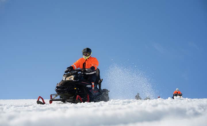 Osoba w pomarańczowym kombinezonie i kasku jedzie skuterem śnieżnym po lodowcu Langjokull.