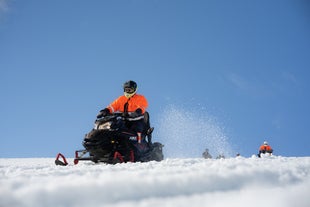 En person i orange overall och hjälm kör snöskoter över Langjokull-glaciären.