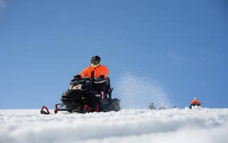 En person i oransje kjeledress og hjelm kjører snøscooter over Langjokull-breen.