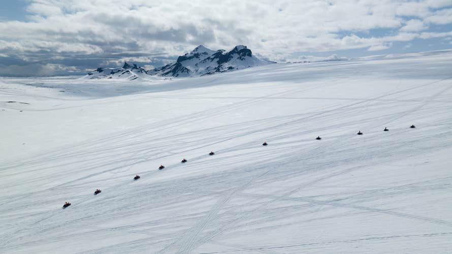 Eine Reihe von Schneemobilen auf einem verschneiten Gletscher in Island.