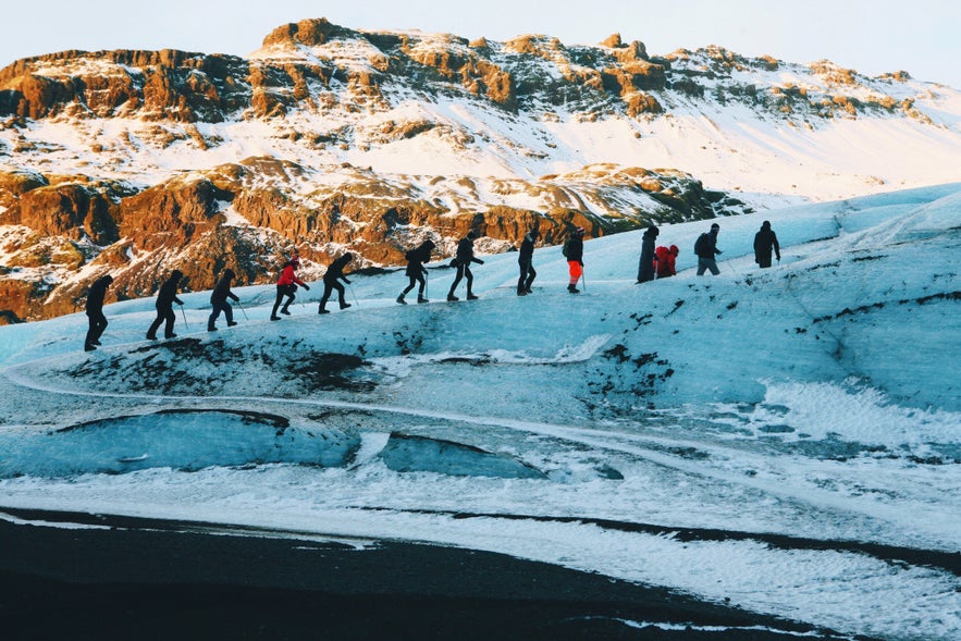 Grupa turystów podąża za przewodnikiem w górę Solheimajökull.