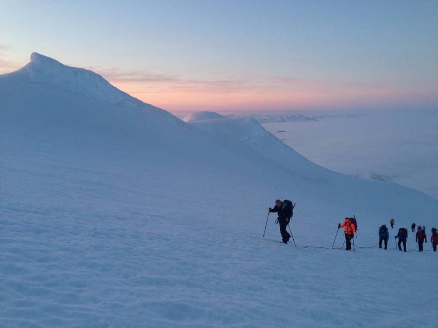 A line of hikers climbing the snowy summit dome of Snaefellsjokull Glacier at sunset