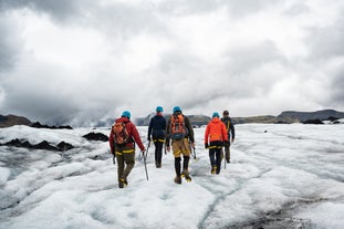 People walk along the vast icy expanse of the Solheimajokull glacier during a guided hike.