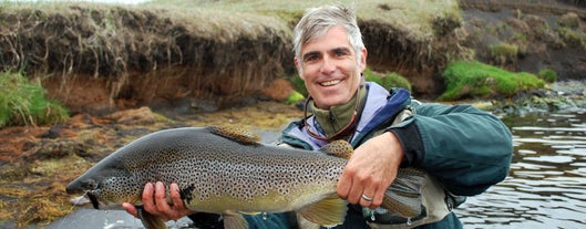 A man smiles as he holds up a fish caught on a fishing tour in North Iceland.