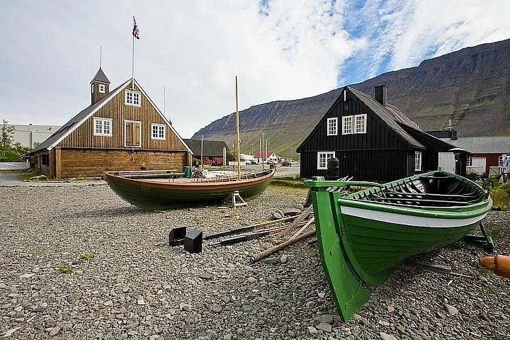 Twee houten boten aan de kust van Isafjordur met een gebouw op de achtergrond.
