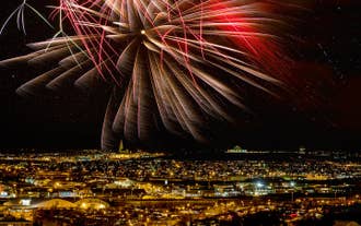 Udsigt til Reykjaviks bylys med et imponerende nytårsfyrværkeri, der oplyser den stjerneklare nattehimmel ovenover.