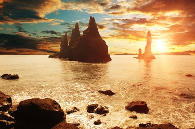 アイスランド南海岸にあるレイニスドランガル（Reynisdrangar）の岩柱群に、夏の夕日が沈んでいく光景。