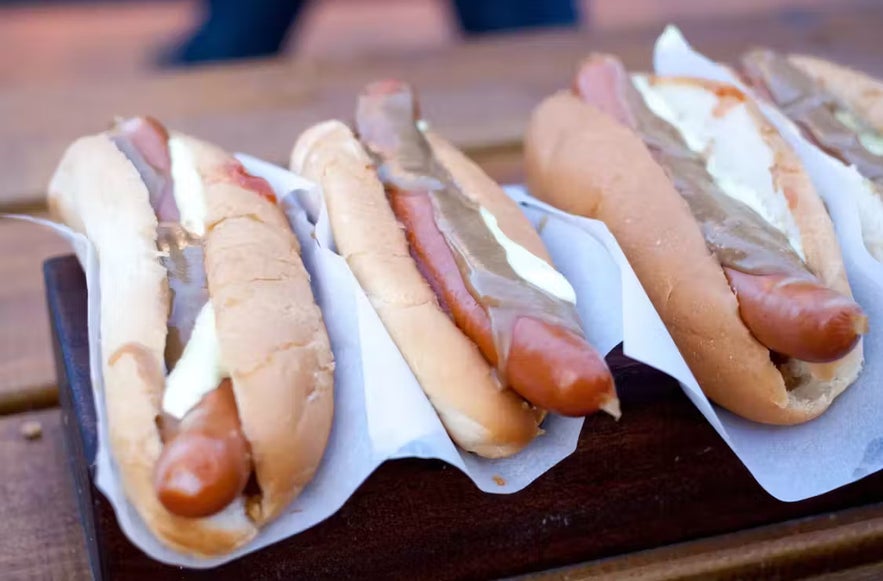 Icelanders eat traditional hot dogs with crispy onions and sauces at a Reykjavik Street Food Stall.