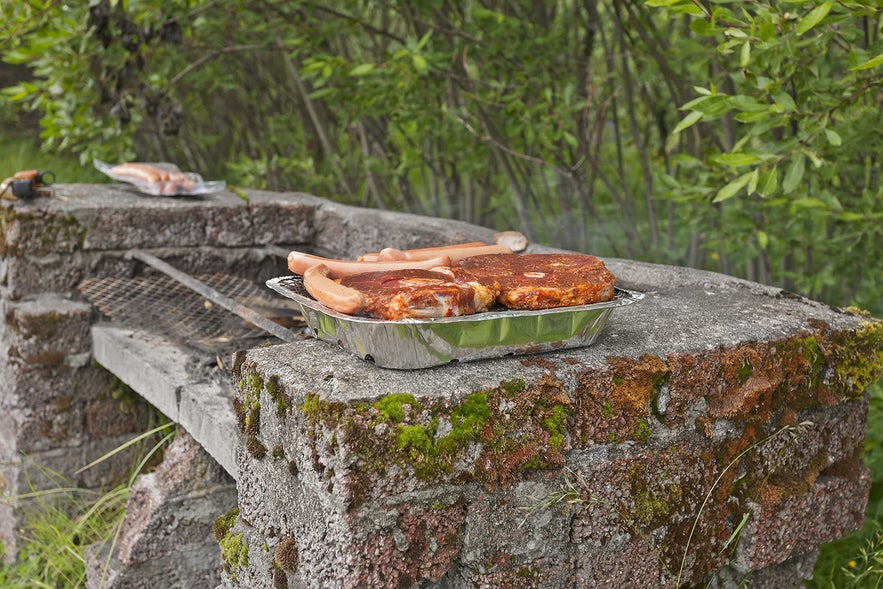 Icelanders grill marinated meat and sausages on outdoor barbecue in Icelandic nature.