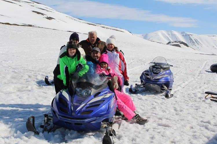 En gruppe mennesker stiller op til et billede på en snescooter under en tur i Island.