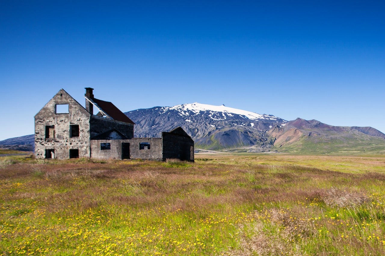The glacier-capped Snaefellsjokull volcano looks majestic with an abandoned building in the foreground.